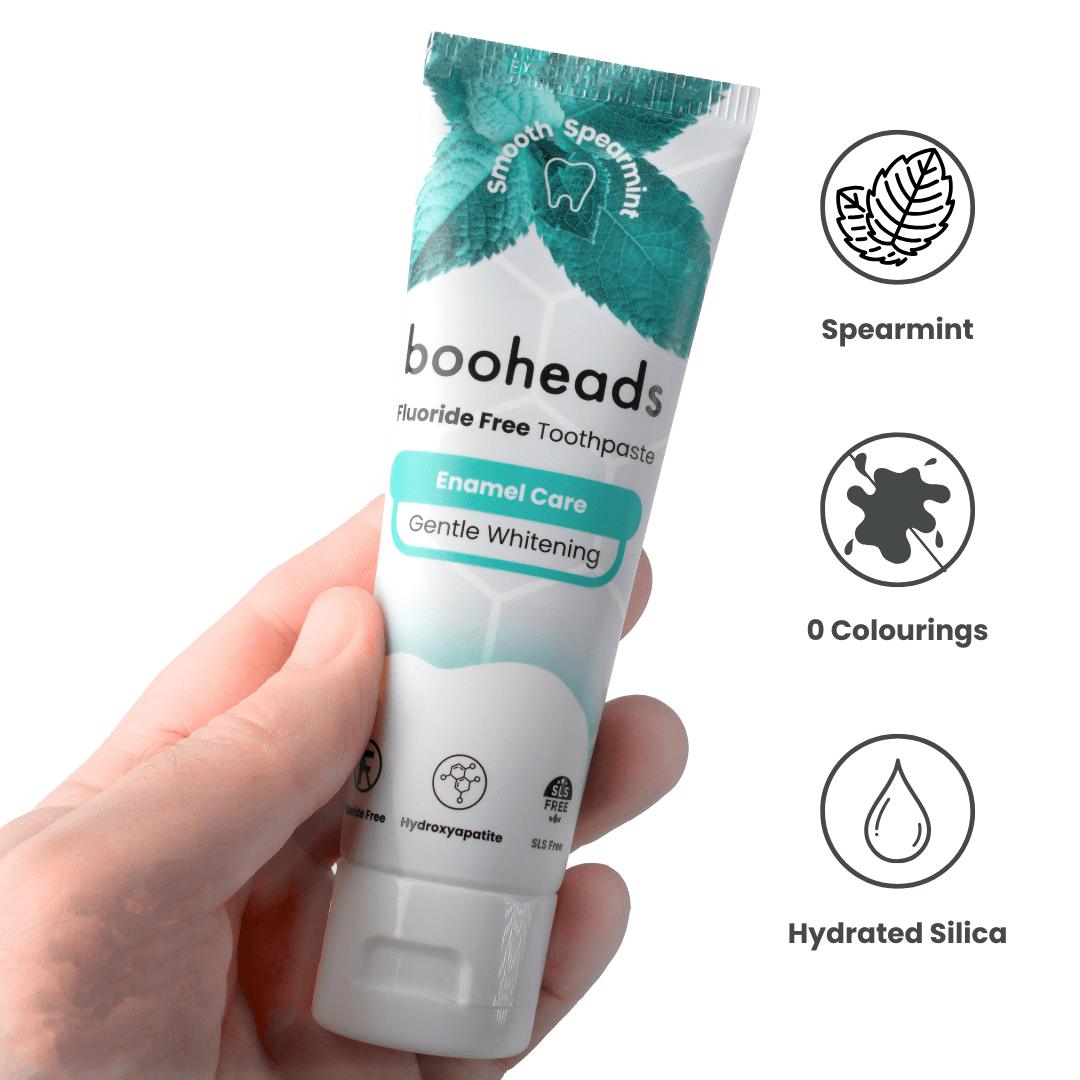 Hand holding a tube of booheads toothpaste with product details on a white background