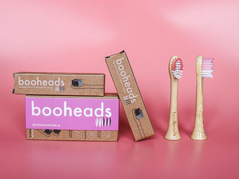 Booheads biodegradable bamboo electric toothbrush heads with eco-friendly cardboard packaging, displayed against a pink background to highlight sustainable oral care.