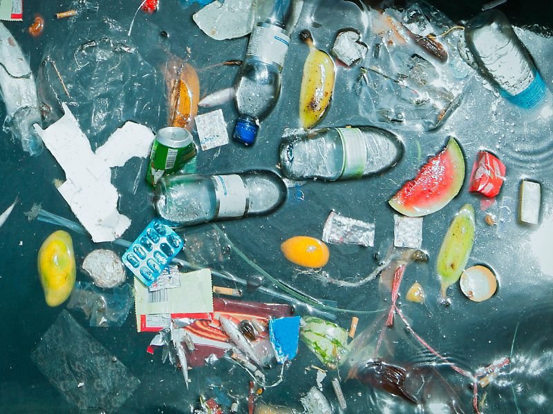 Assorted plastic bottles, food waste, and packaging floating in polluted water, highlighting the environmental impact of single-use plastics.