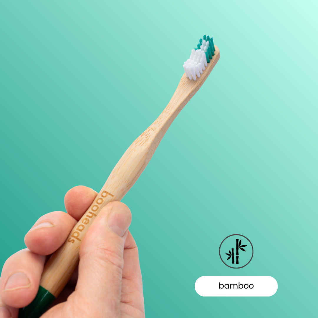Hand holding a booheads bamboo toothbrush on a teal background