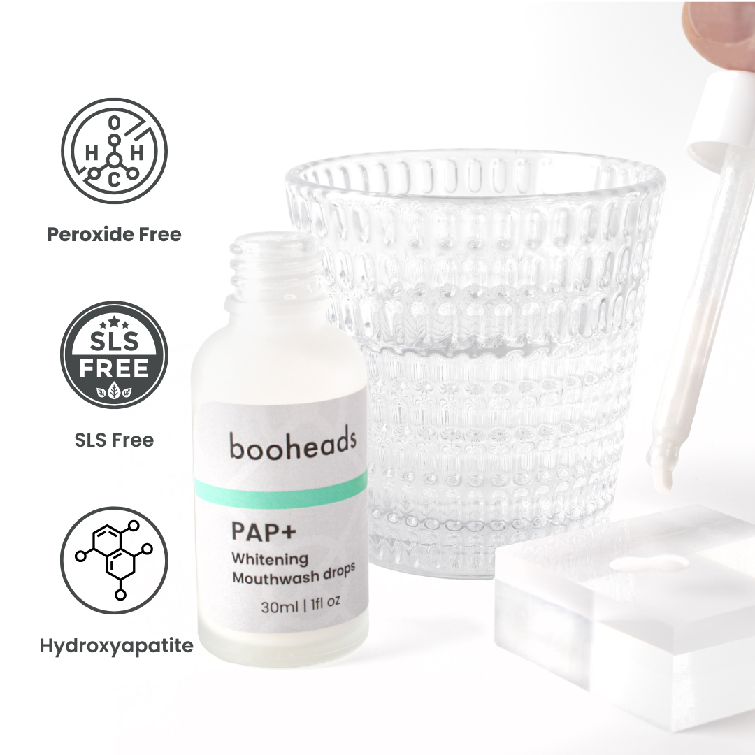 booheads PAP+ Whitening Mouthwash Drops shown beside a glass of water with benefit icons