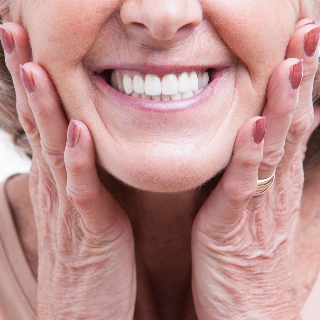 Close-up of an elderly woman's face with hands on cheeks, showing a smile.